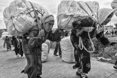 Two elderly women walk toward the Melilla crossing point carrying on their backs heavy bales of merchandise. Usually this transport is performed from some warehouses located several kilometers away from the border. Melilla. Spain