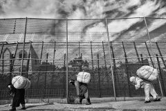Three women bend their bodies forward because of the heavy goods loaded in their back. They walk towards the border between Spain and Morocco. Melilla. Spain